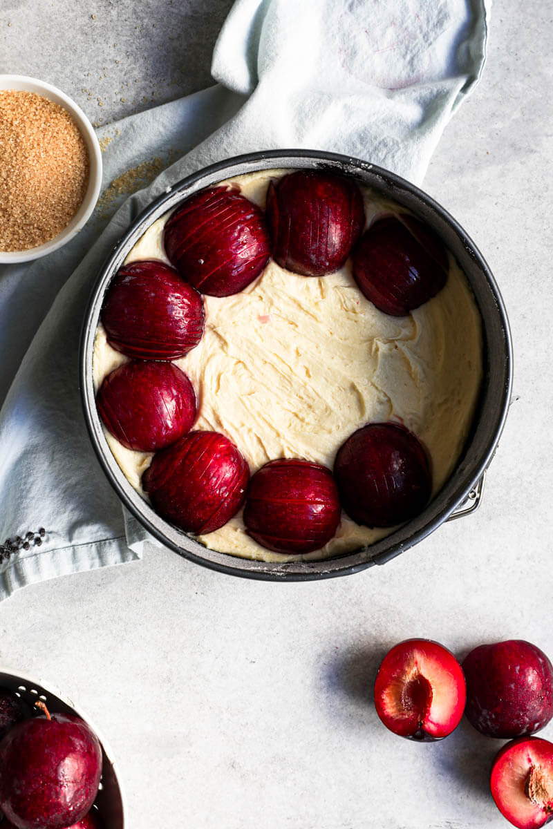 Overhead shot of the cake pan filled with the cake batter topped with some of the plums