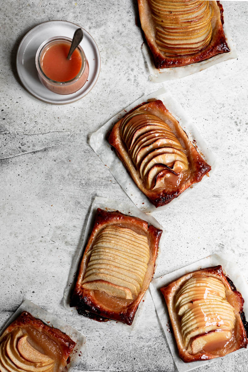 Overhead shot of the puff pastry apple tarts with a pot of salted caramel in the top left corner