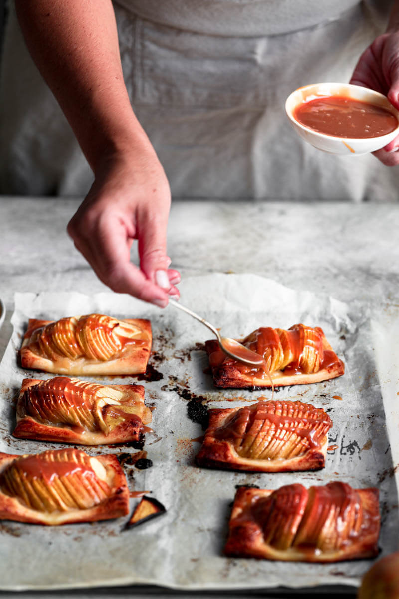 90° shot of a hand drizzling salted caramel sauce over the tarts