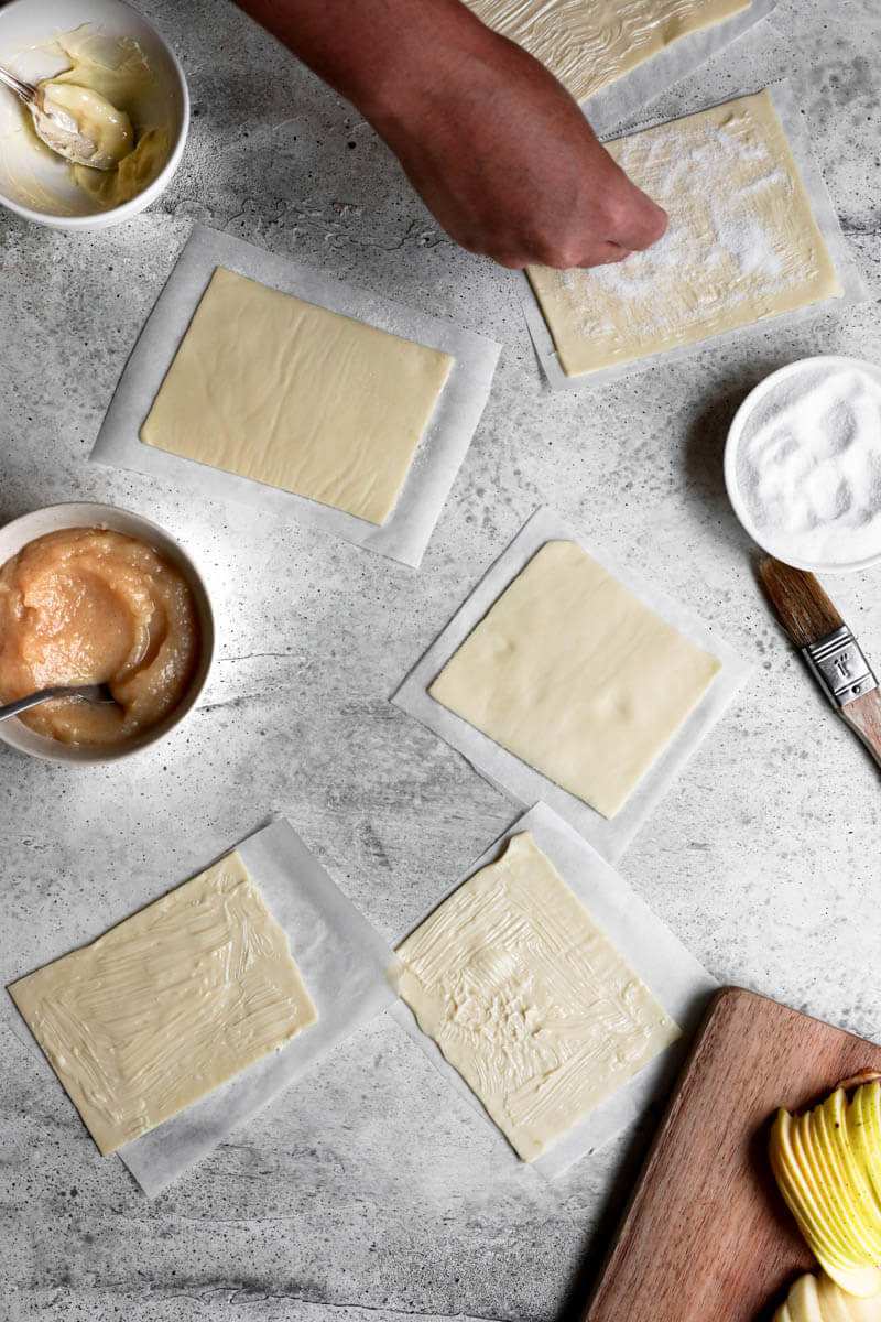 Overhead shot of the puff pastry rectangles with a hand sprinkling sugar over them