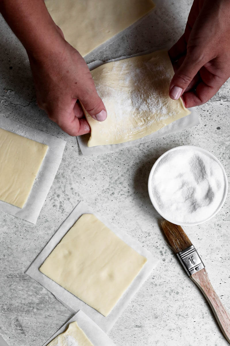 Overhead shot of 2 hands turning over one rectangle of puff pastry dough