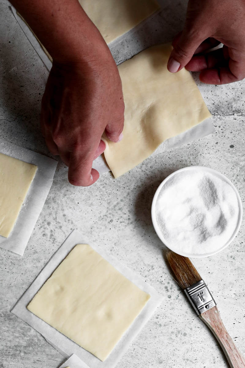 Overhead shot of 2 hands turning over one rectangle of puff pastry dough