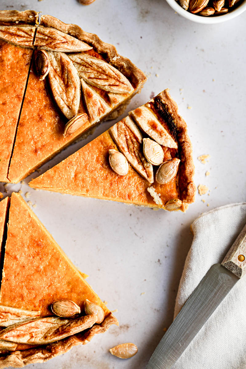 A closeup of the sliced pumpkin ricotta quiche seen from above, with a plate and a pumpkin slice in the top right corner.