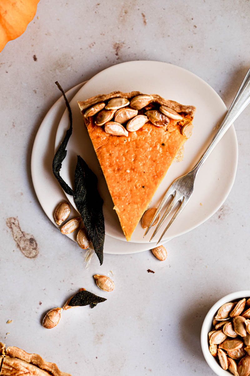 A piece of savory pumpkin pie on a pink plate with a fork on the side and the corner of the quiche in the bottom left corner.