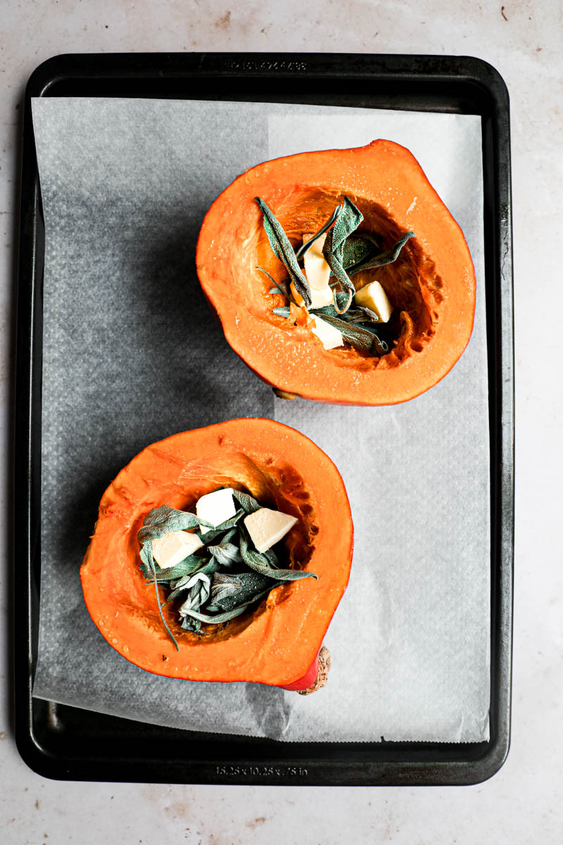 Making the pumpkin quiche filling: a pumpkin cut in 2 on a baking tray lined with parchment paper, each filled with sage and butter.