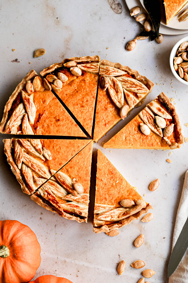 The sliced pumpkin ricotta quiche seen from above, with a plate and a pumpkin slice in the top right corner.