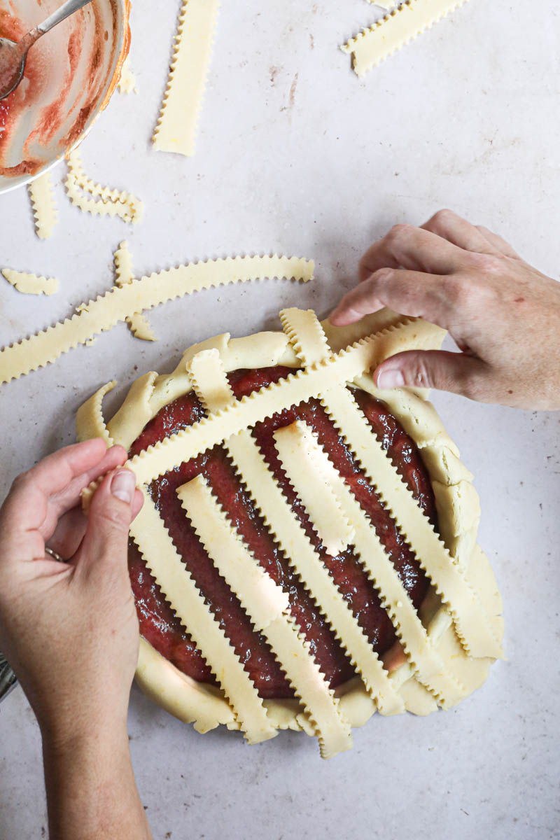 Two hands covering the quince pie with the dough bands forming a lattice top pie.