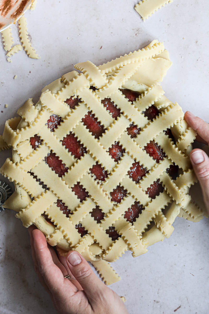 Two hands holding the lattice top quince pie before baking.