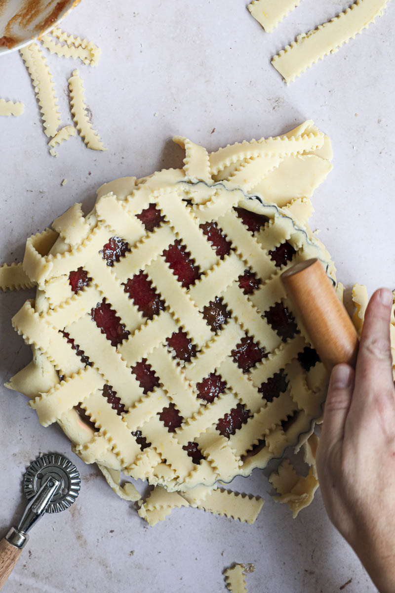 Two hands pressing a rolling pin over the edges of the tart tin to cut off the excess dough.