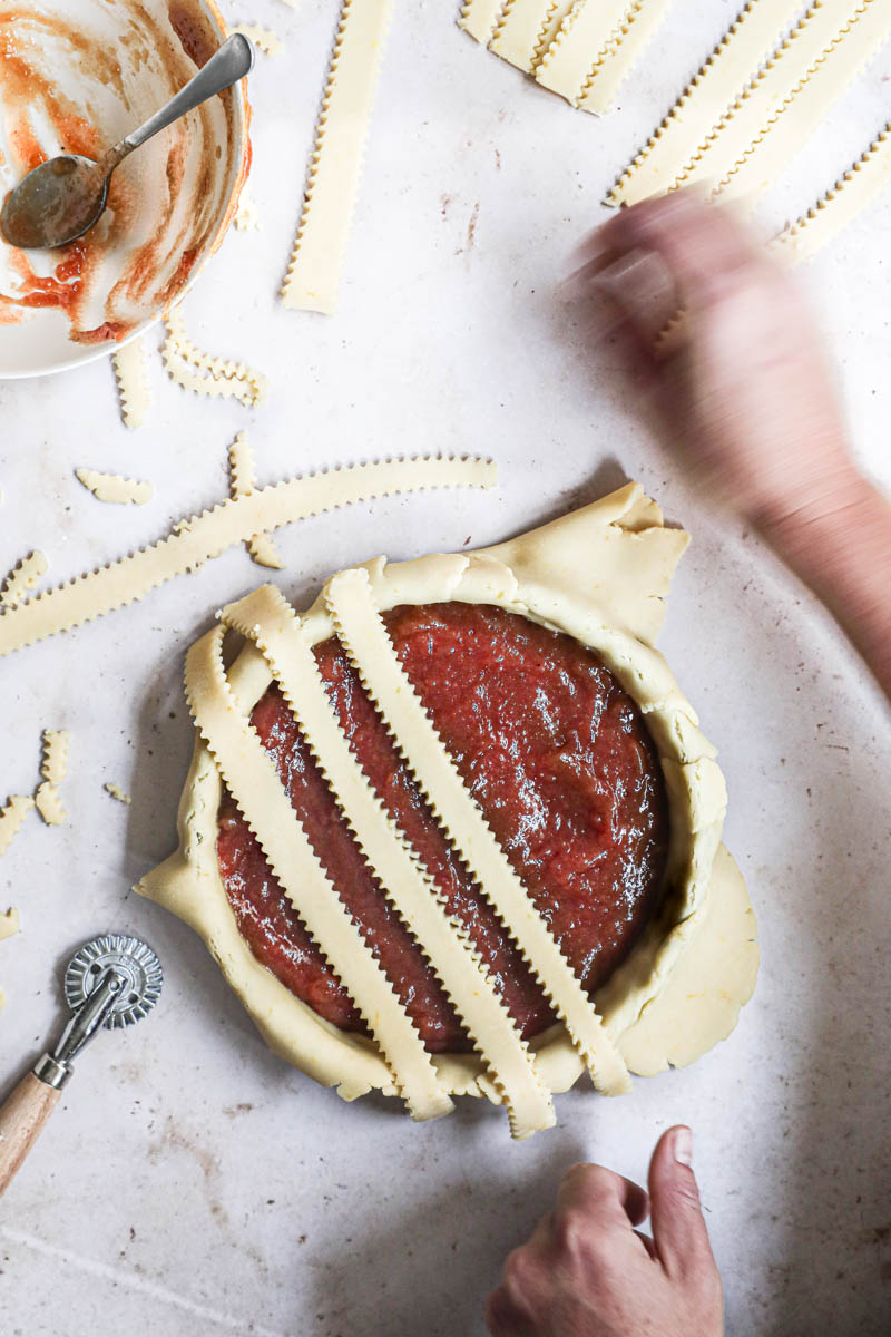 Two hands covering the quince pie with the dough bands forming a lattice top pie.