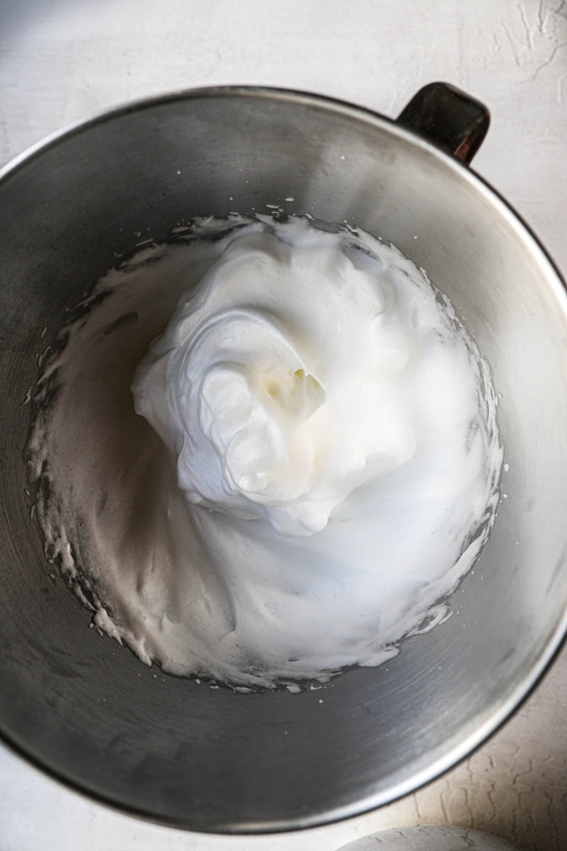 Beaten egg whites for the ladyfinger cake inside a mixing bowl.