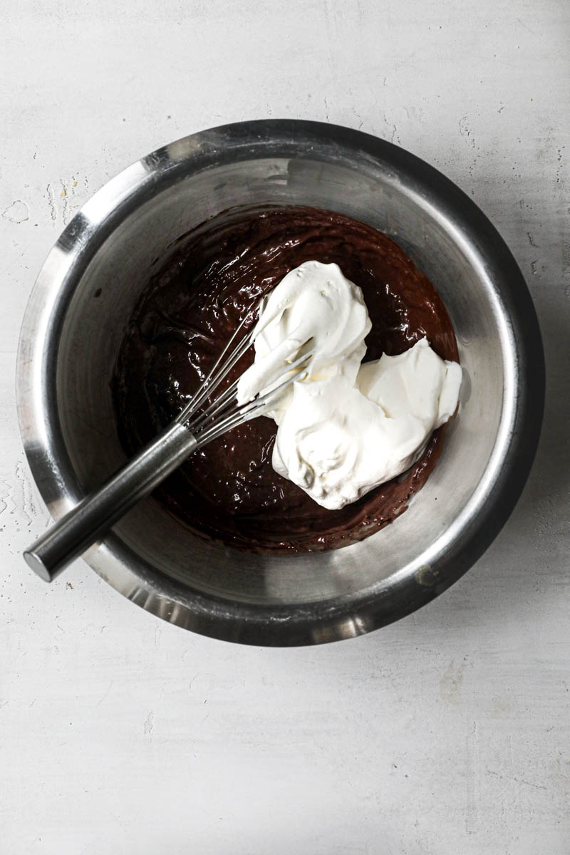 Chocolate ganache in a silver bowl with a small scoop of cream on top and a whisk on the side.
