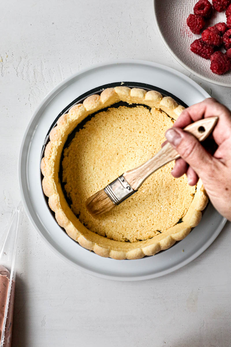 One hand brushing the cake disk with raspberry syrup.