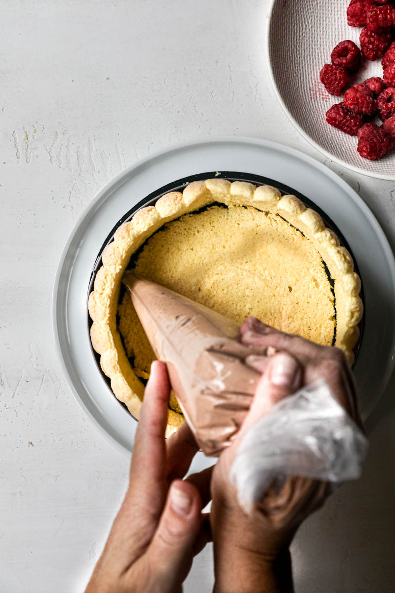 Two hand Piping the chocolate Bavarian cream into the sides of the raspberry chocolate charlotte.