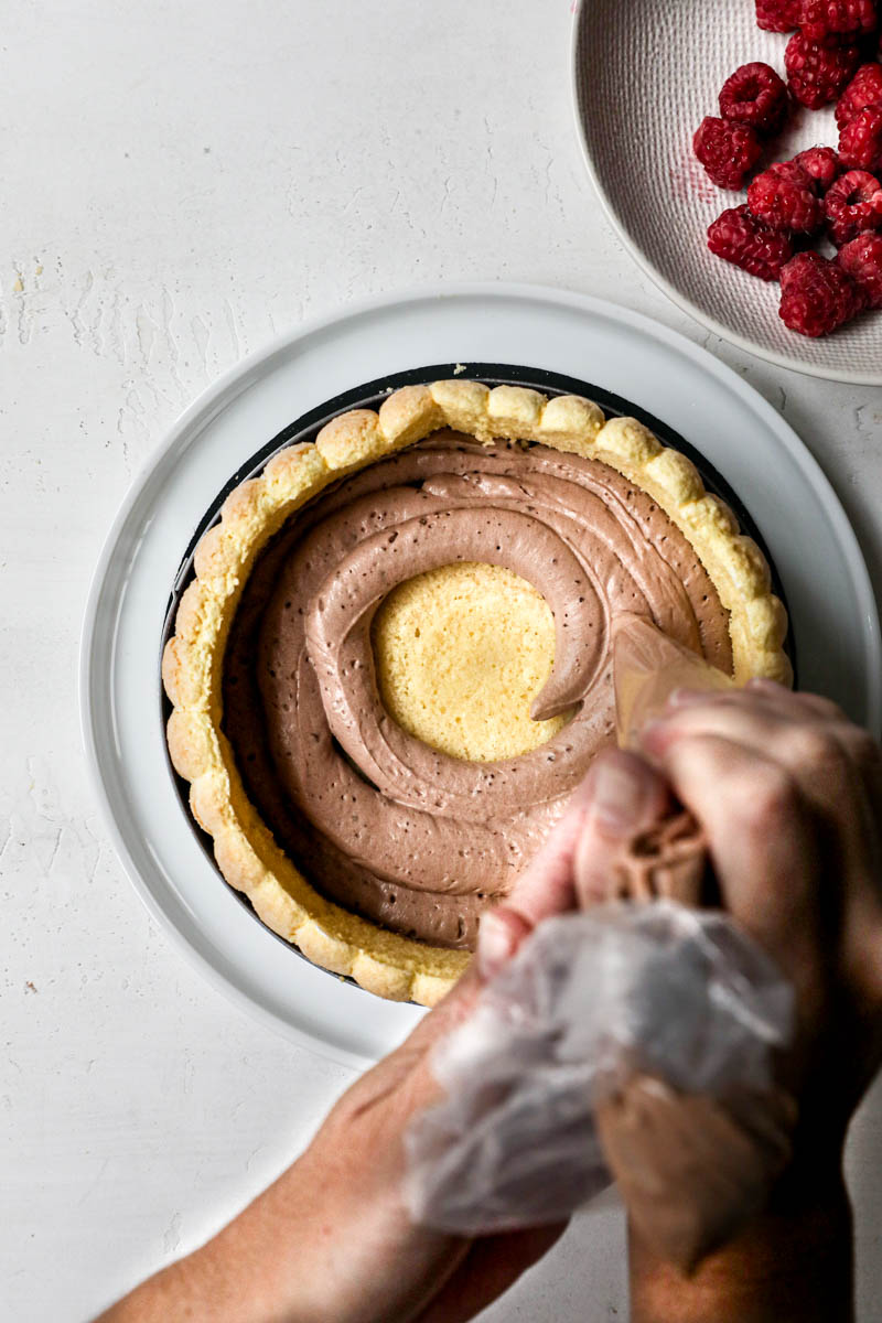 Two hand Piping a layer of chocolate Bavarian cream into the raspberry chocolate charlotte.