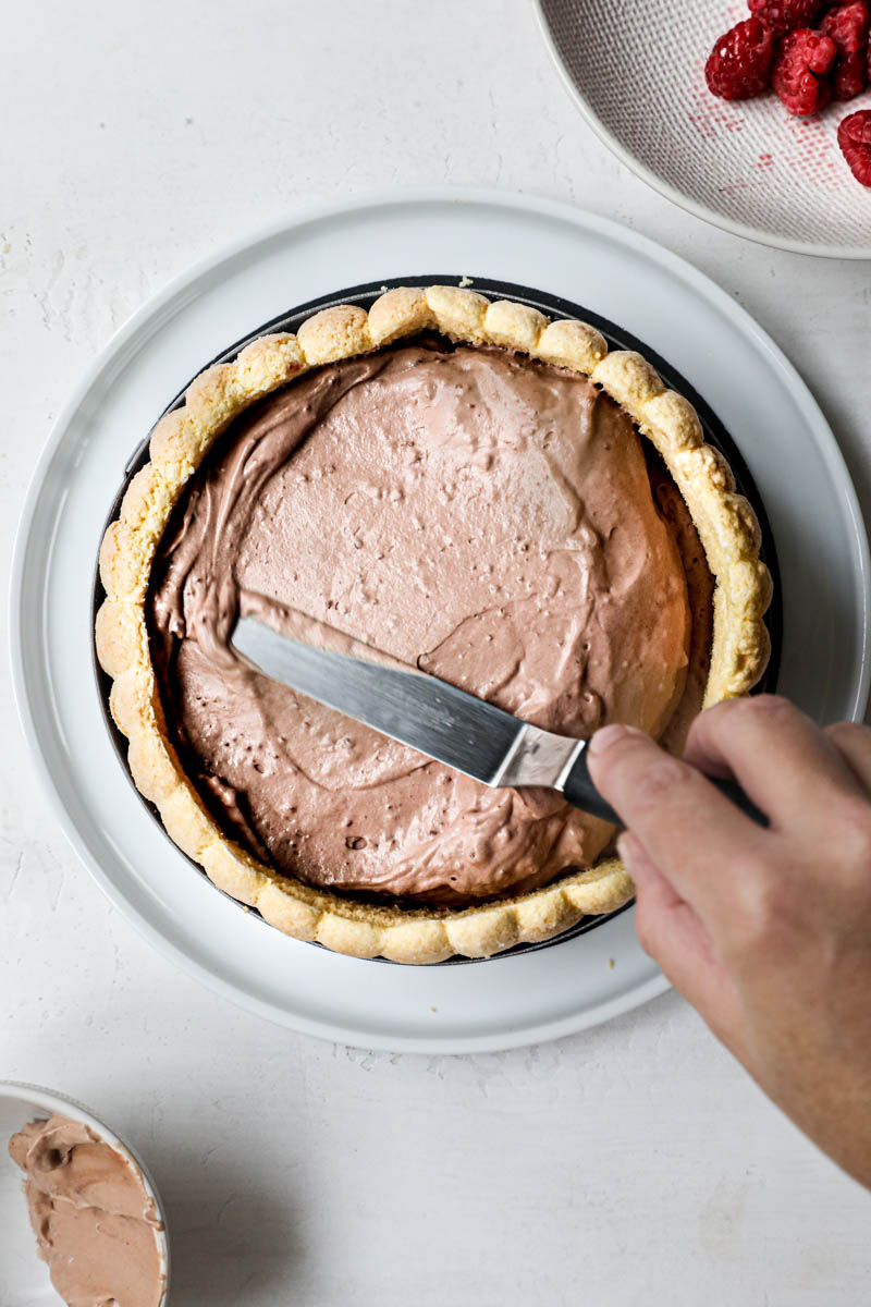 One hand spreading the Bavarian cream on top of the charlotte cake with a small offset spatula.