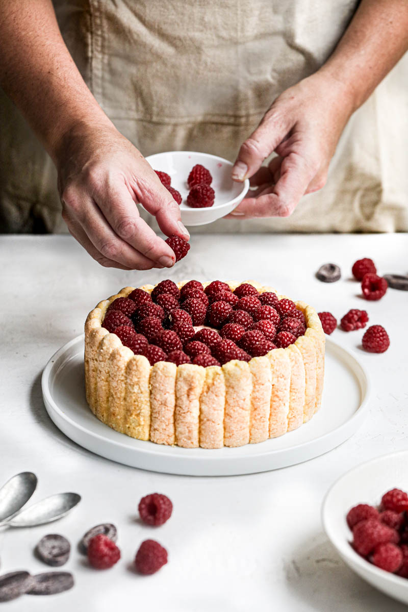 One hand placing a raspberry on top of the chocolate charlotte cake.