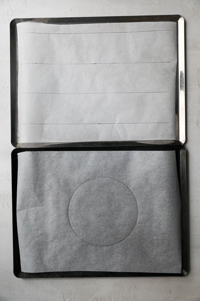 2 baking tray lined with parchment paper with a circle and 2 bands drawn over it.