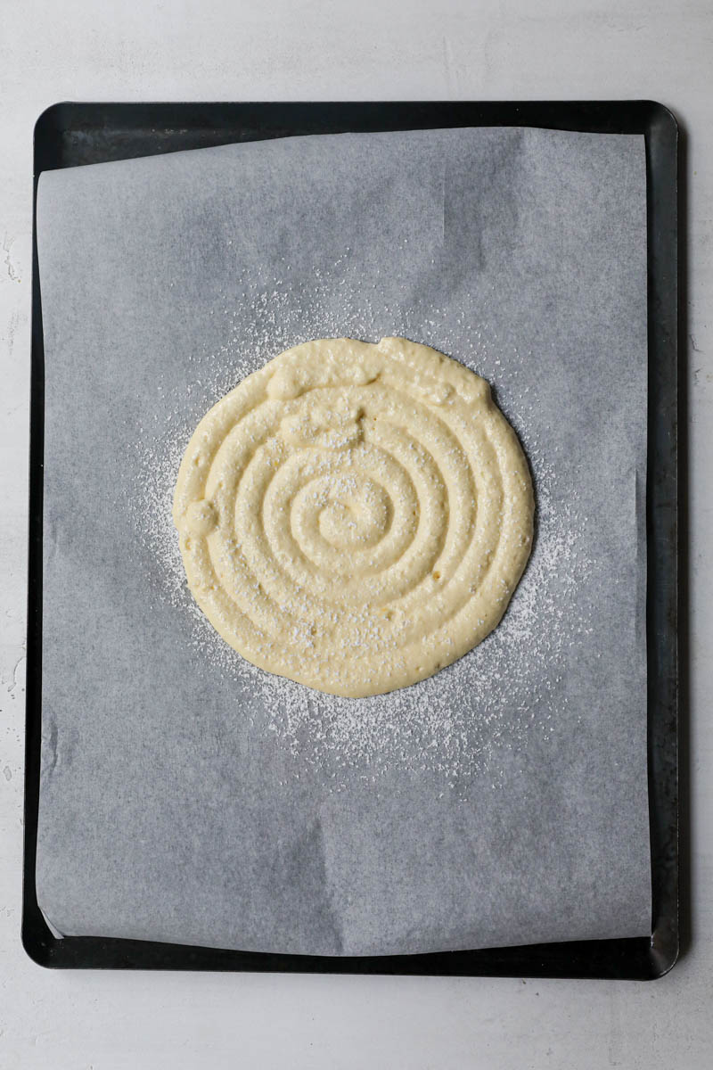 1 16 cm disk of ladyfinger batter piped out on a piece of parchment paper.