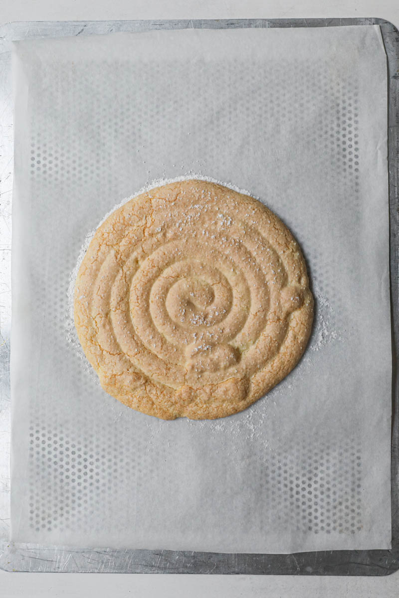 The baked disk of ladyfinger cake on a piece of parchment paper.