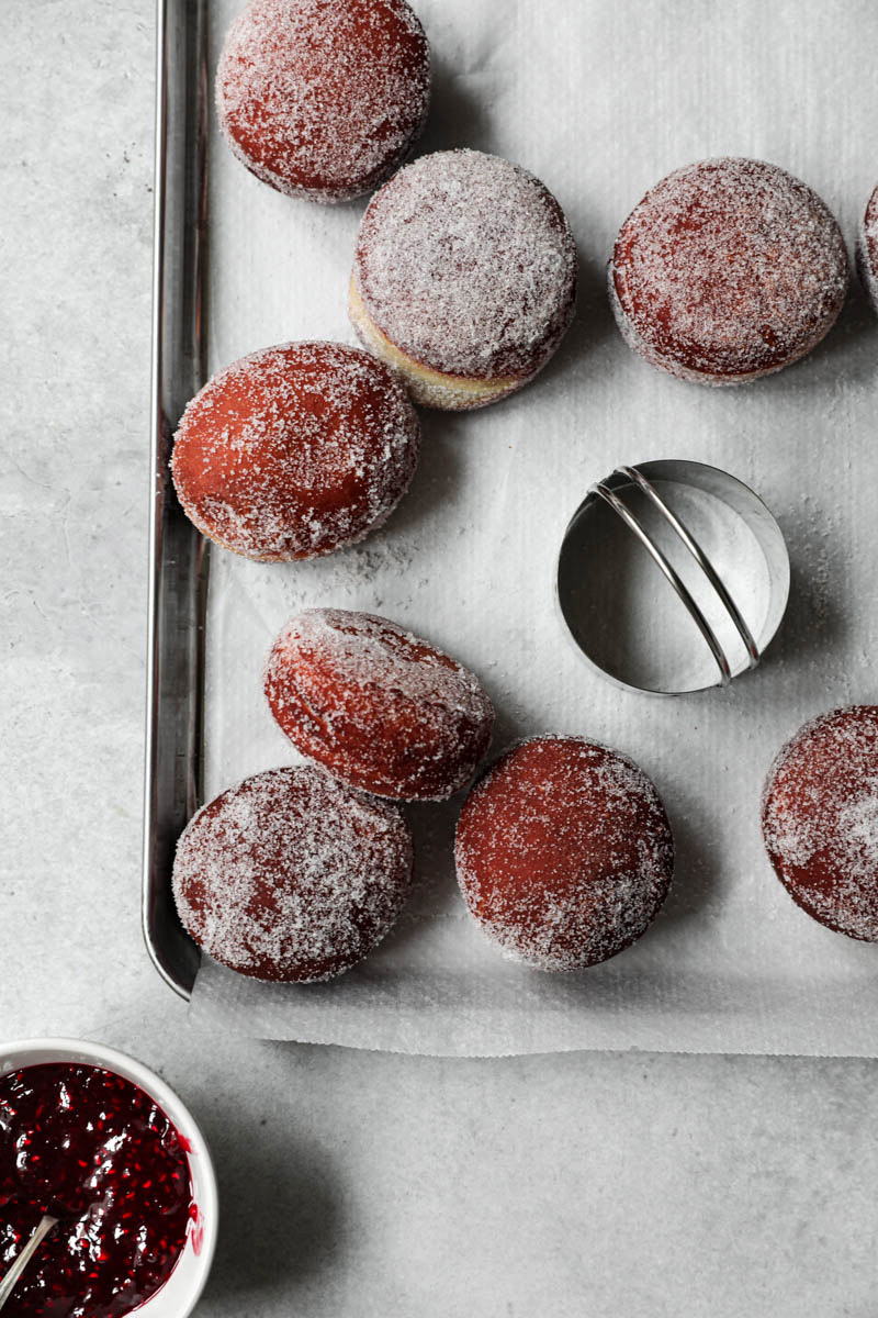 Sugar coated donuts on a baking tray with the cutter on it.