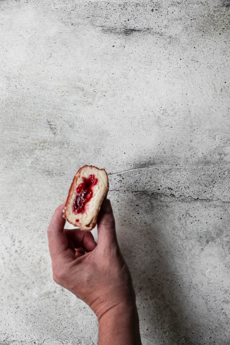 A hand holding a sliced filled raspberry jam brioche donut.