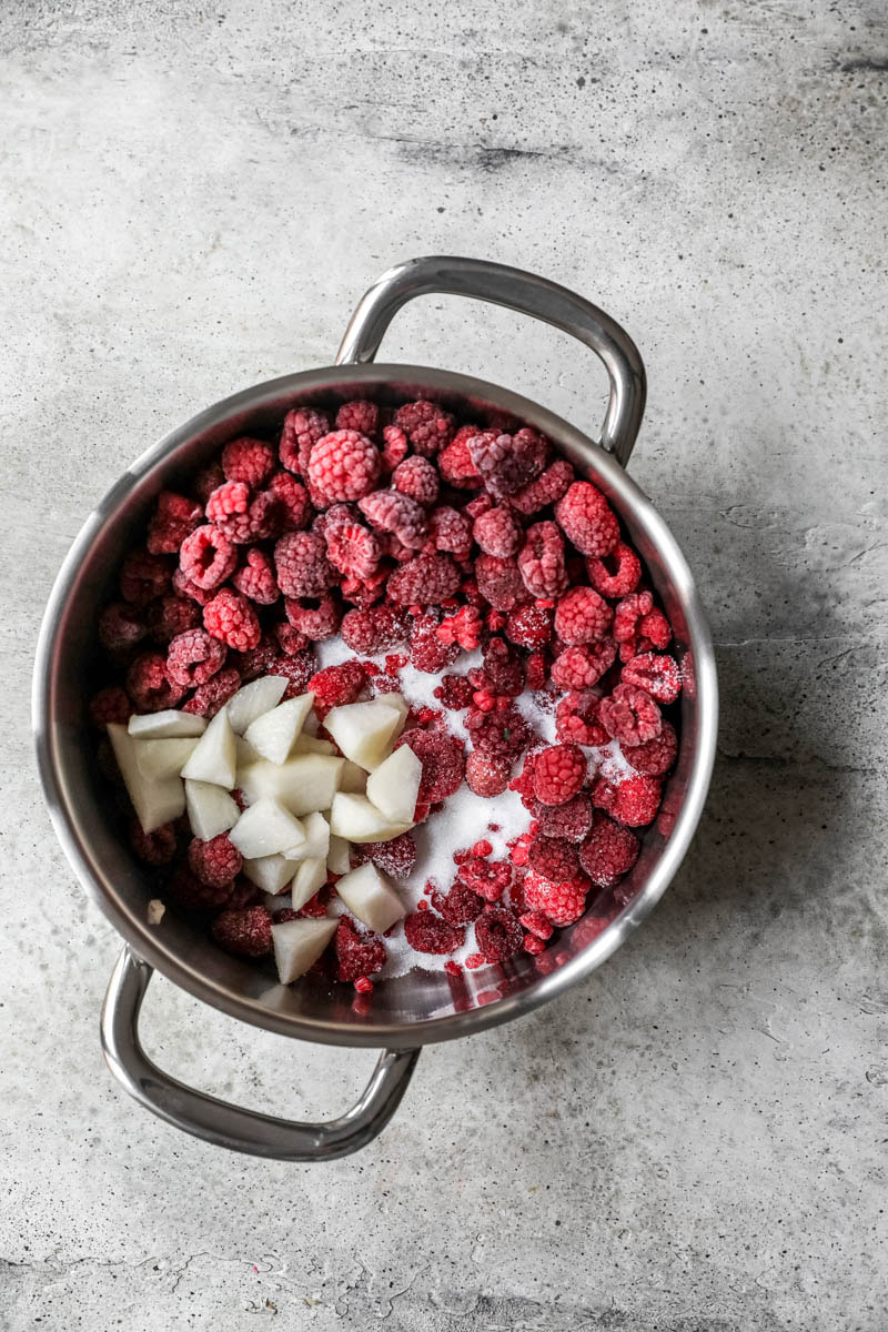 A big pot with frozen raspberries and sliced pear.