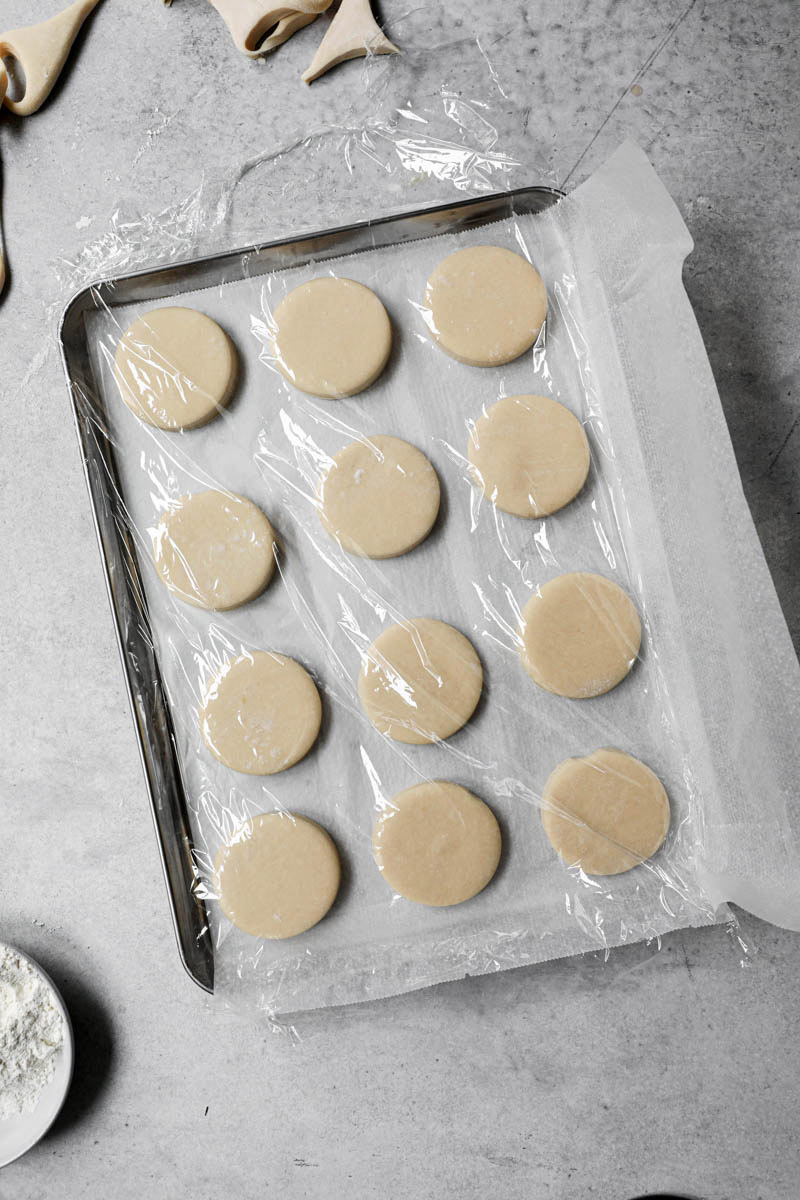 Shaped donuts on a baking tray lined with parchment per covered with film wrap.