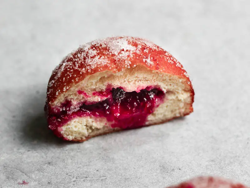 Closeup of a sliced filled raspberry jam brioche donut.