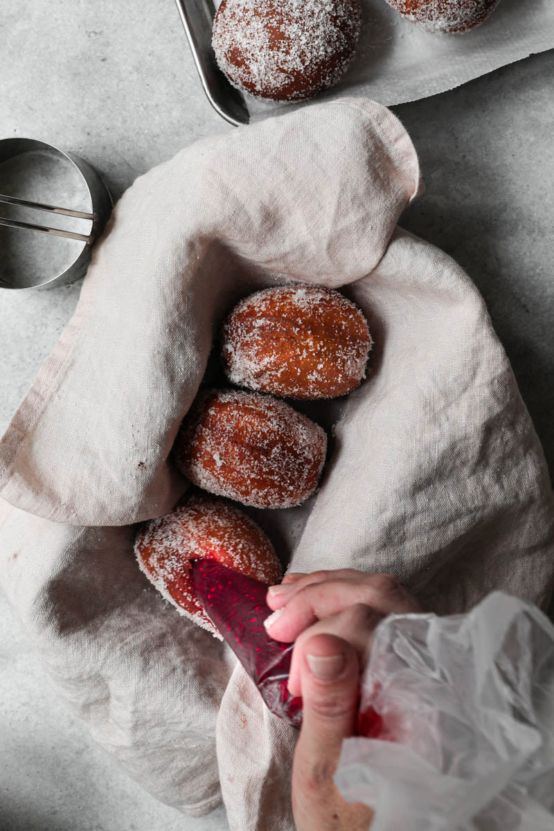 A hand filling the donuts using a piping tip.