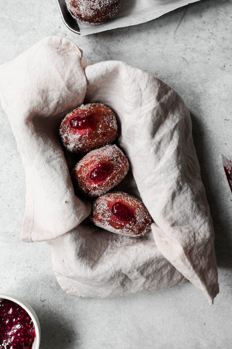 3 donuts filled with raspberry jam inside a pan lined with a pink cloth.