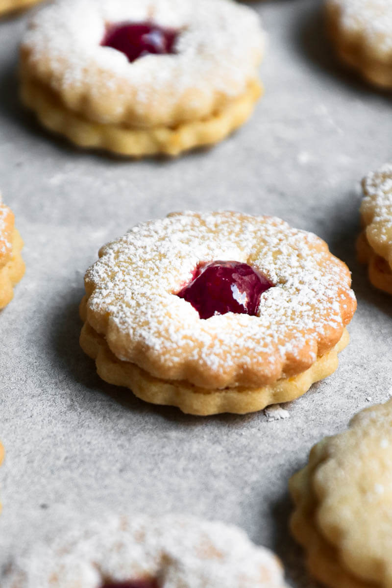 One linzer cookie filled with raspberry jam, with other blurry all around