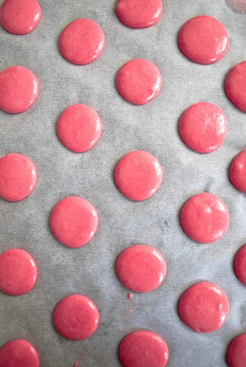 Raspberry macaron shells piped on parchment paper
