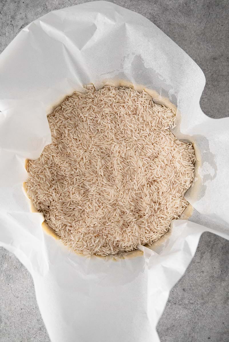 Shortbread crust in the tart tin lined with parchment paper filled with rice for blind baking