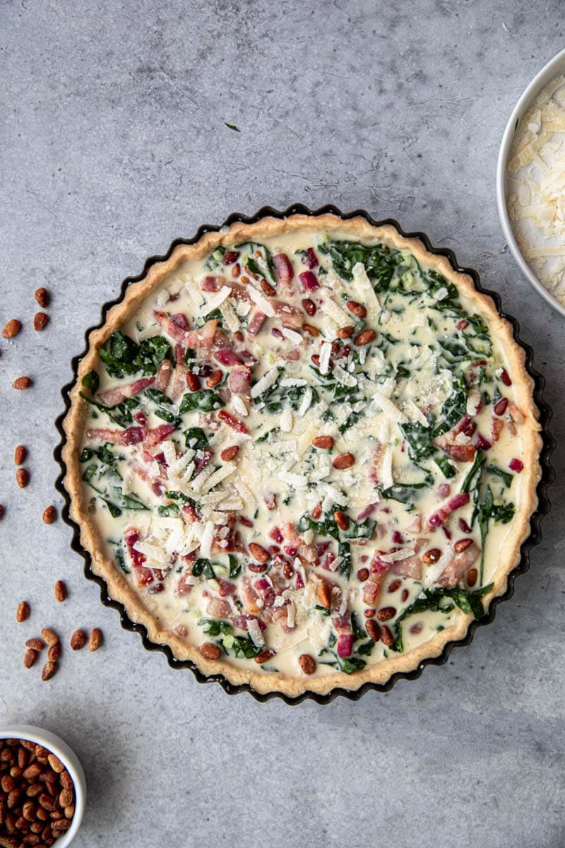 Pour the quiche batter over the filled quiche crust until the filling is covered. Top with the rest of the parmesan and the roasted pine nuts.