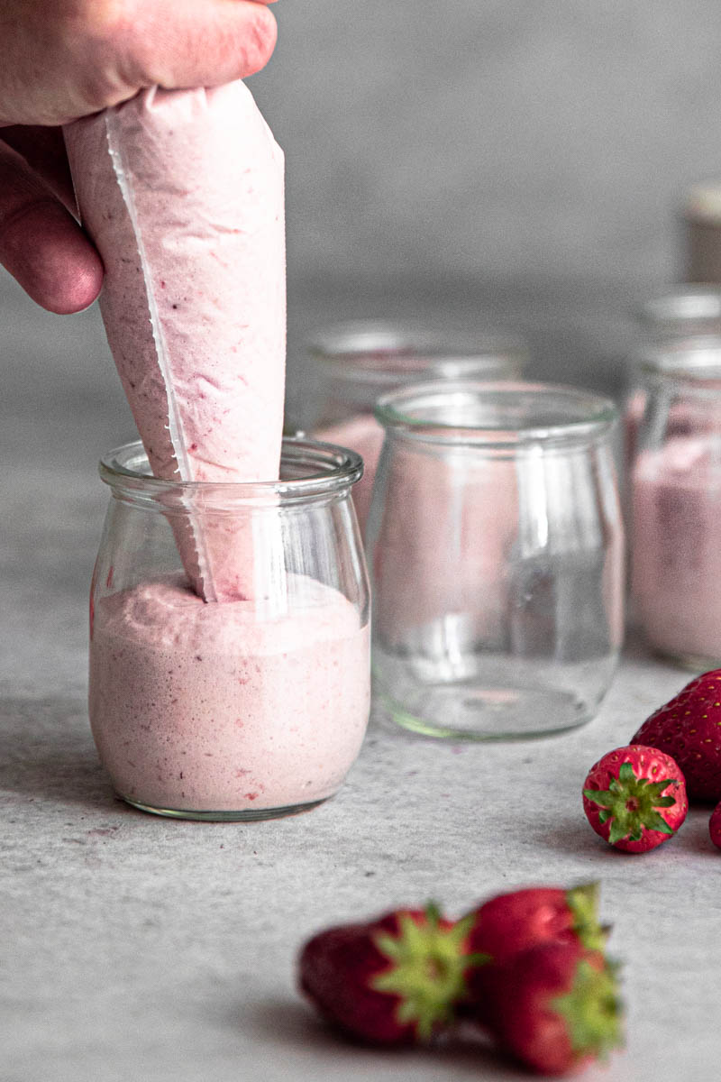 One hand filling the jars with the simple strawberry mousse using a piping bag.