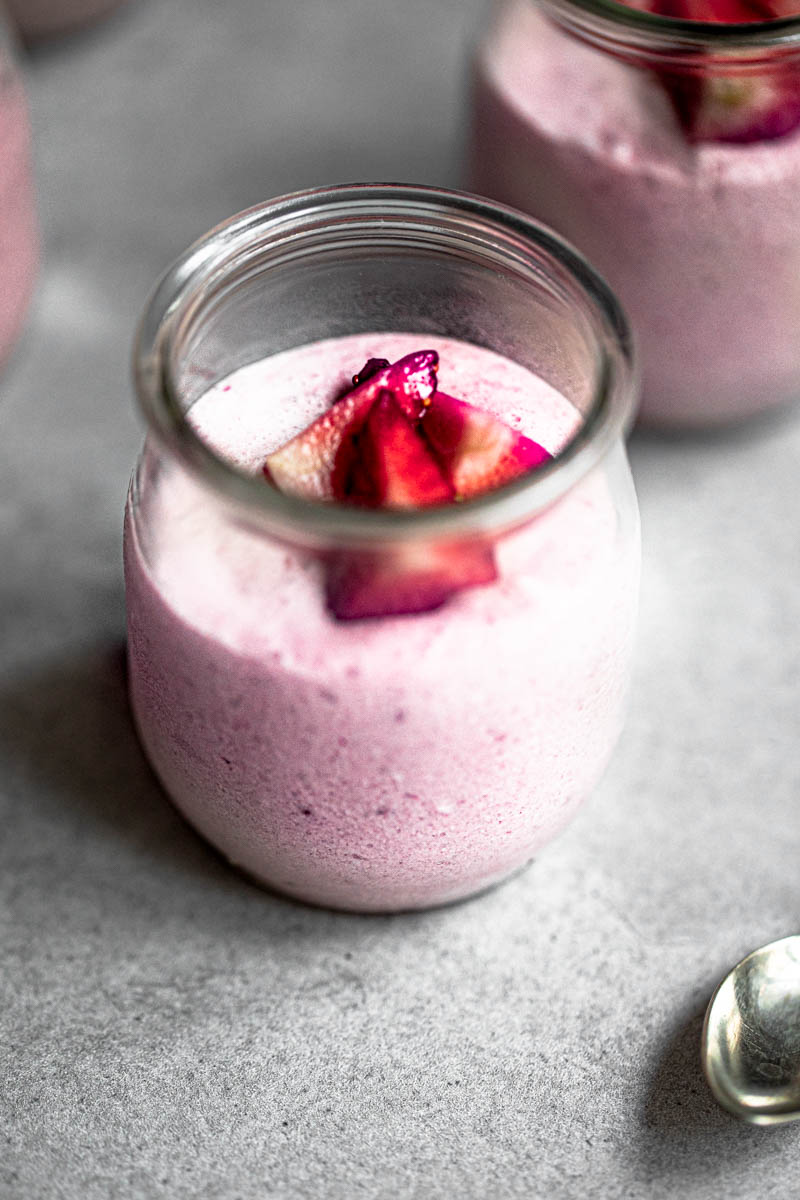 One strawberry mousse inside a glass jar topped with strawberries.