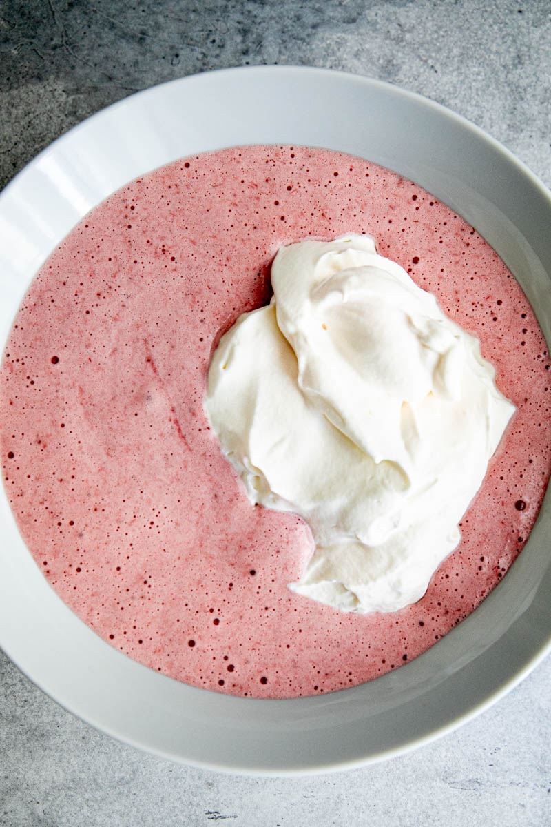 Strawberry curd plus whipped cream inside a bowl ready to be mixed to make strawberry mousse.