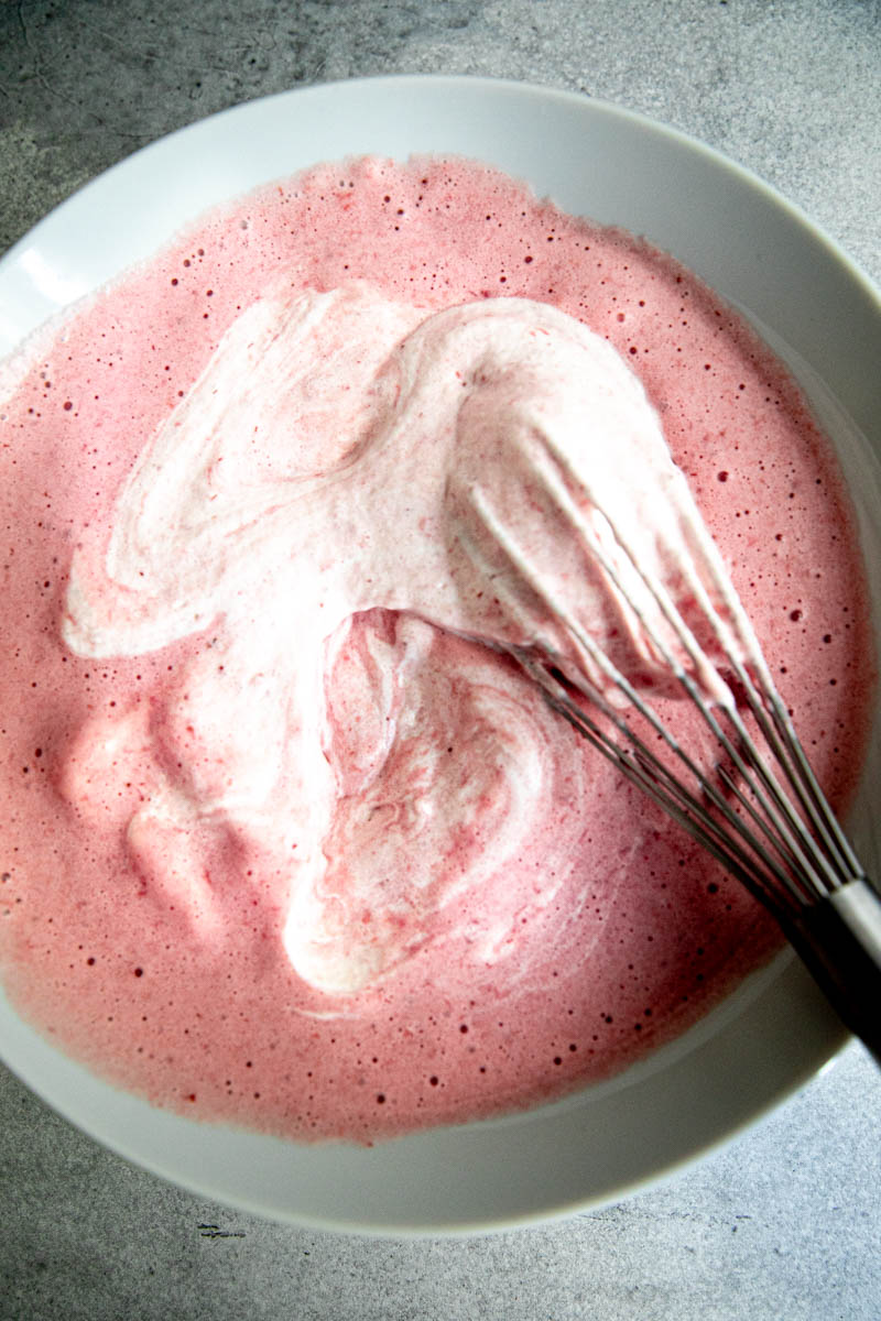 The strawberry mousse being mixed inside a white bowl.