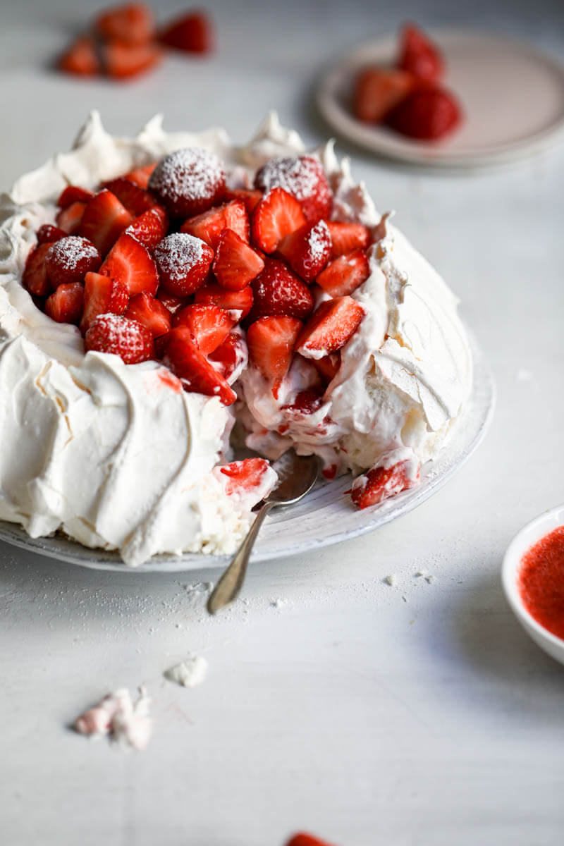 45° shot of the strawberry pavlova missing one slice with a small spoon on the serving plate