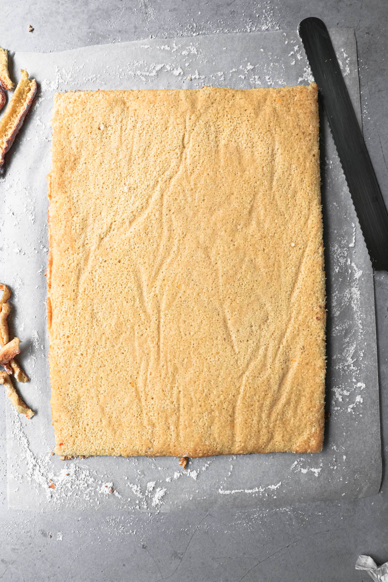 The roll cake turned on a paper covered in powdered sugar with the edges trimmed.