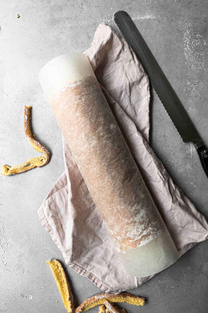 The cake rolled and covered in parchment paper with strawberries on the side.