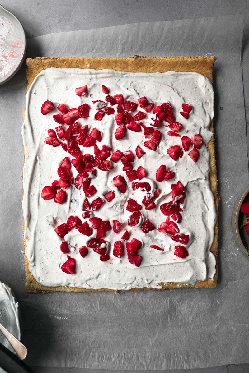 The unrolled cake filled with strawberry Chantilly cream with a small bowl with diced strawberries on the top left corner.