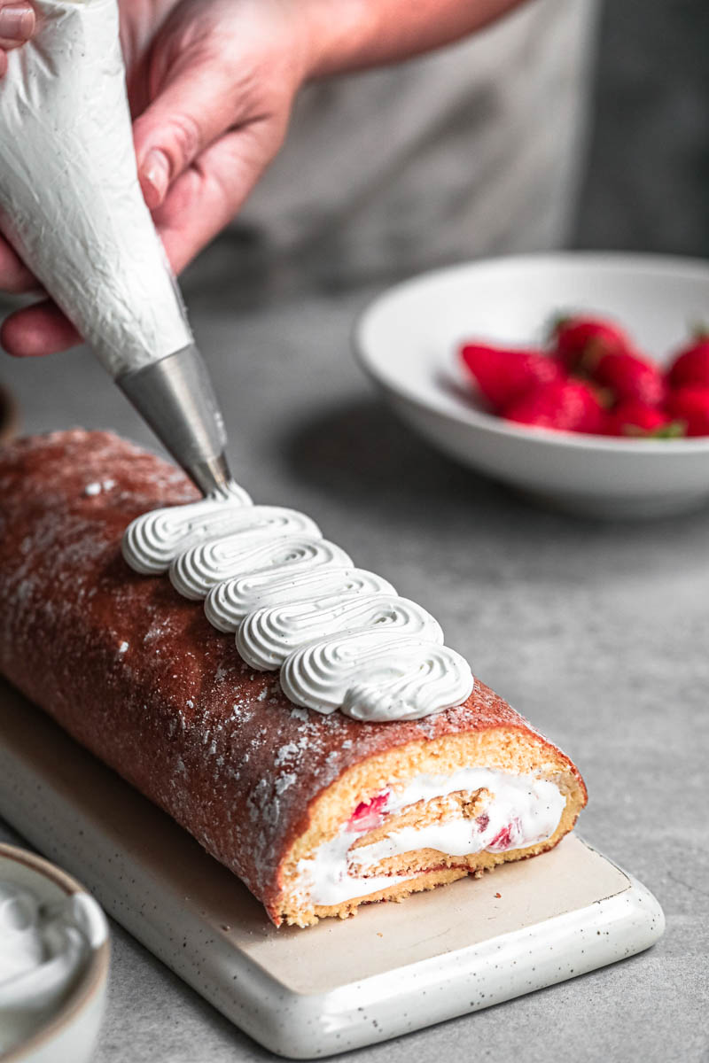 One hand piping Chantilly cream on top of the strawberry roll cake.