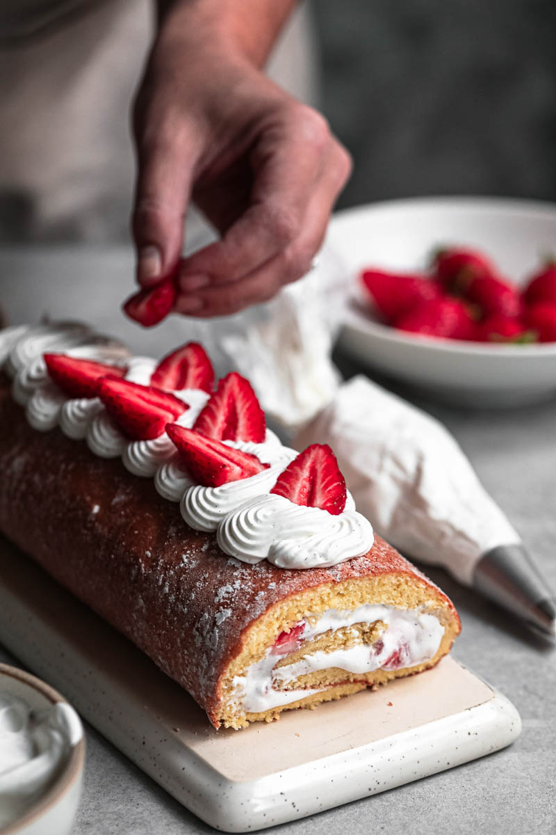 One placing fresh strawberries on top of the strawberry roll cake covered with Chantilly cream.