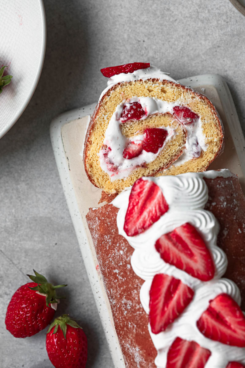 Closeup of the strawberry roll cake with a slice cut off as seen from above.