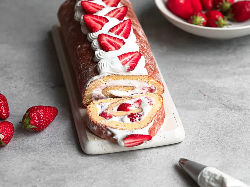 The strawberry roll cake on a rectangular plate, with one slice cut off so we can see the inside.