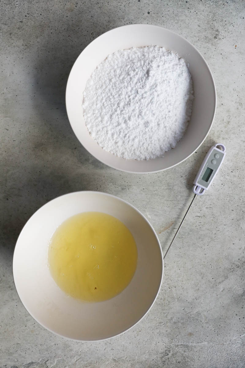 One bowl with raw egg whites, a second bowl with powdered sugar.