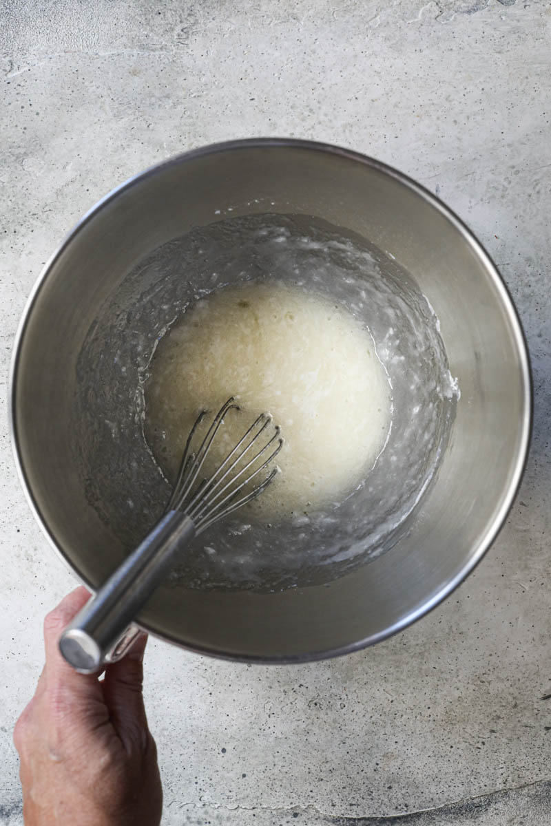 The egg whites and the sugar mixed inside a mixing bowl with a whisk inside.