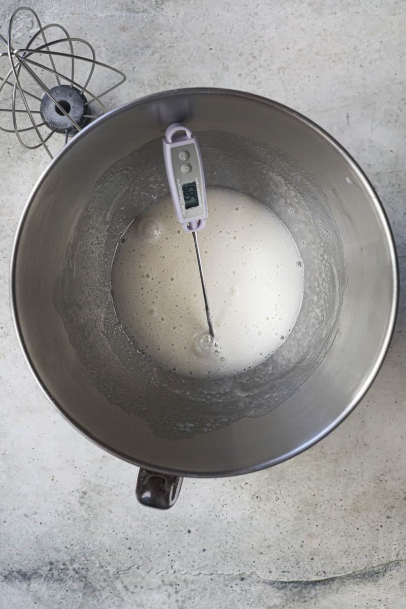 The egg whites and the sugar inside a mixing bowl with a thermometer inside.